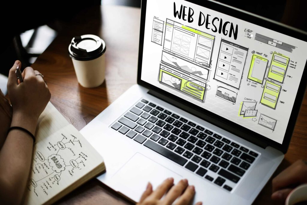 Laptop zeigt Webdesign-Entwürfe, während jemand Notizen macht, um eine Website zu planen, passend zum Thema