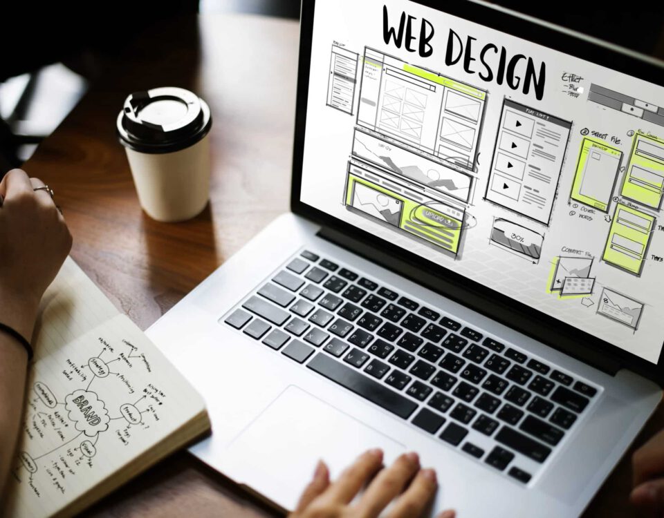 Laptop zeigt Webdesign-Entwürfe, während jemand Notizen macht, um eine Website zu planen, passend zum Thema "Visitenkarte oder Serviceportal".