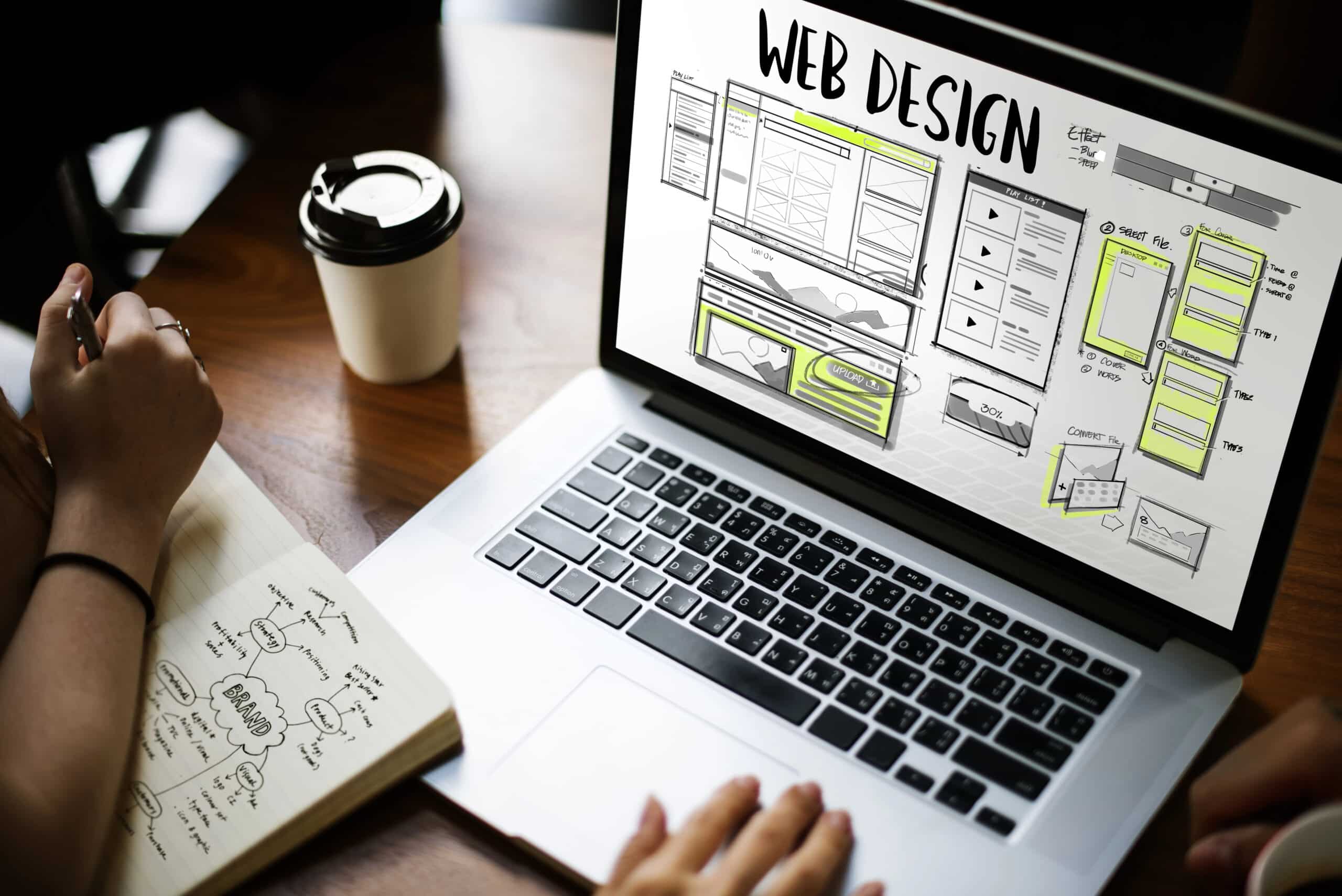 Laptop zeigt Webdesign-Entwürfe, während jemand Notizen macht, um eine Website zu planen, passend zum Thema "Visitenkarte oder Serviceportal".