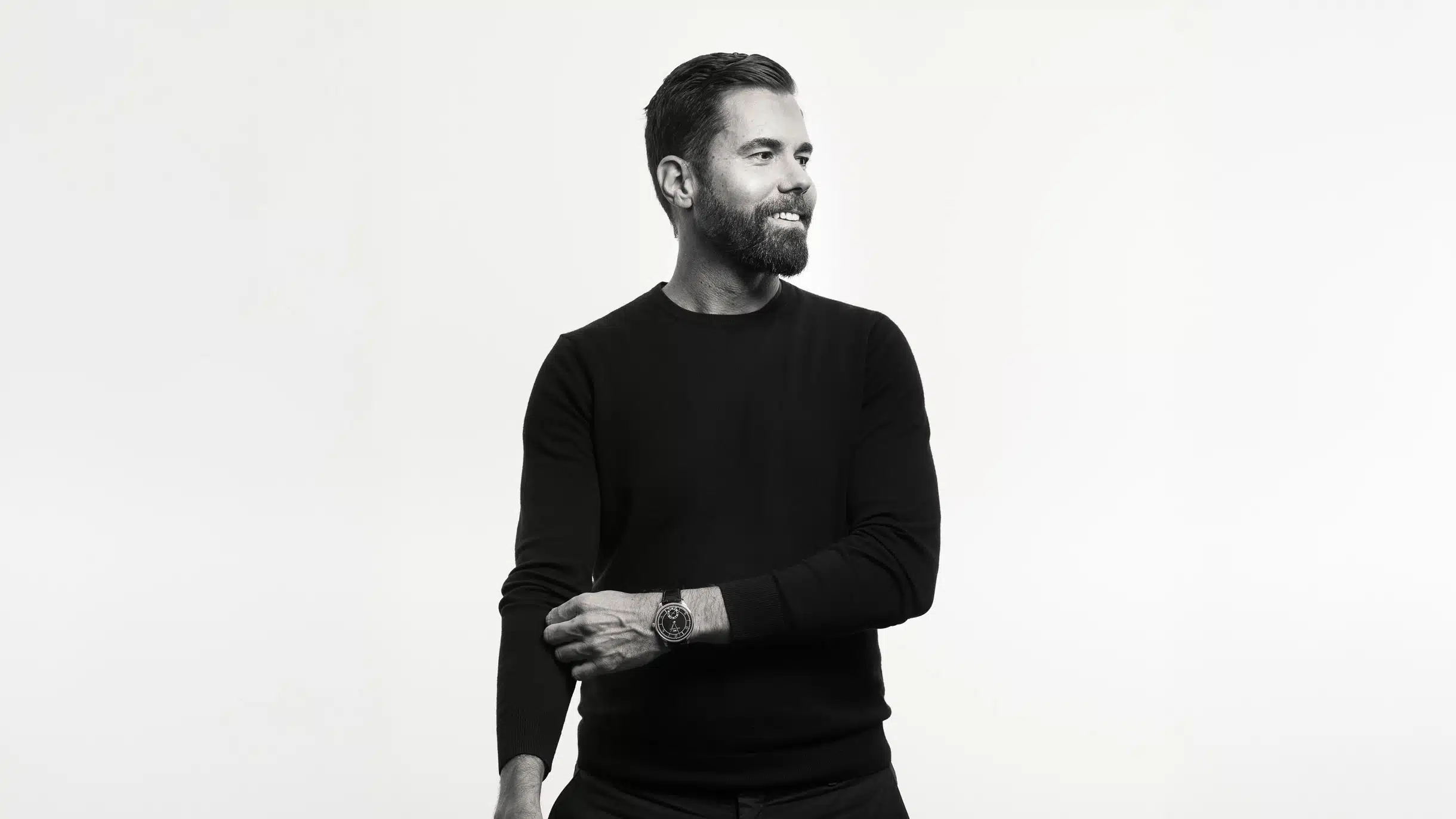 Mann mit Bart und schwarzem Pullover lächelt und schaut zur Seite vor neutralem Hintergrund. Mann mit Bart und schwarzem Pullover lächelt und schaut zur Seite vor neutralem Hintergrund.